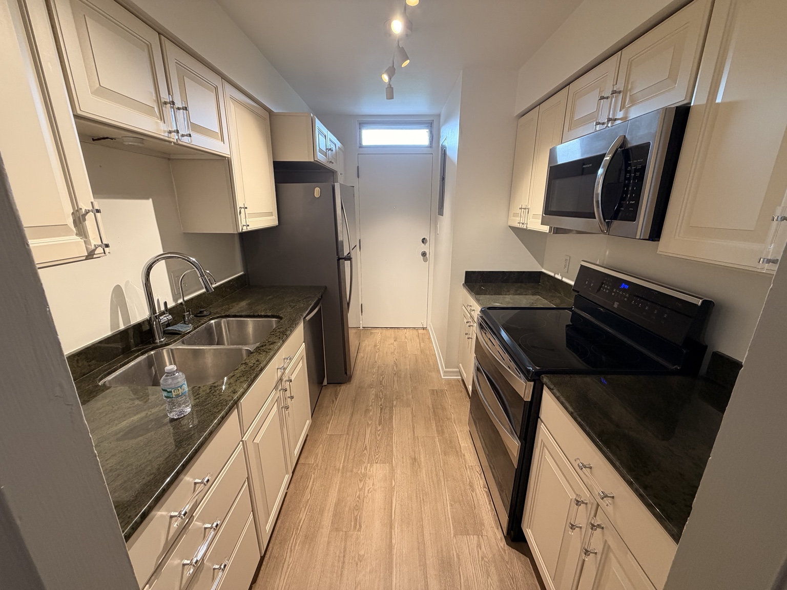 Kitchen with dark counters, an over-range microwave and track lighting